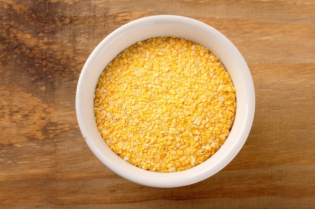 Raw cornmeal flour used in polenta in ceramic bowl over rustic wooden table