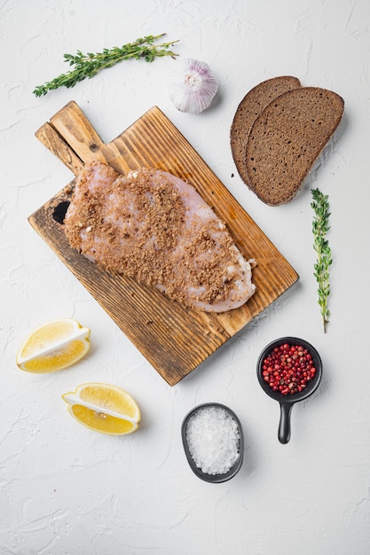 Raw crumbet chicken fillet with ingredients on white table, top view