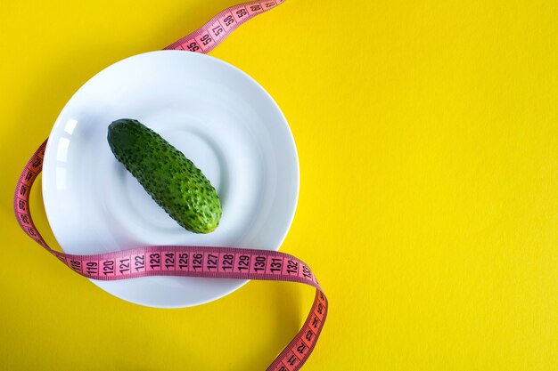 Raw cucumber in the white plate and pink centimeter on the yellow surface.Top view.Copy space.