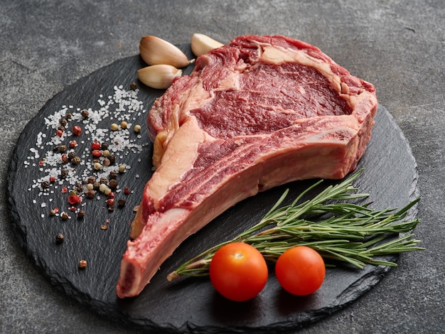 Raw dry aged beef tomahawk steak on slate board with rosemary salt and pepper