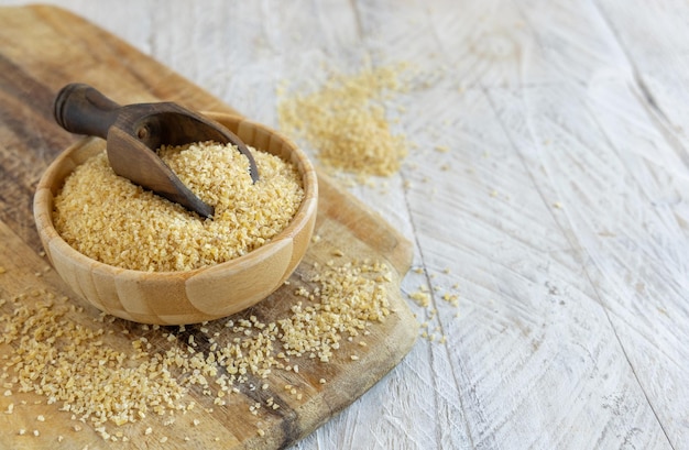 Raw Dry bulgur wheat grain in a wooden bowl with a scoop close up copy space