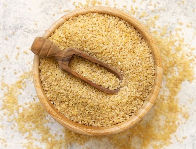 Raw Dry bulgur wheat grain in a wooden bowl with a scoop top view Mediterranean cuisine