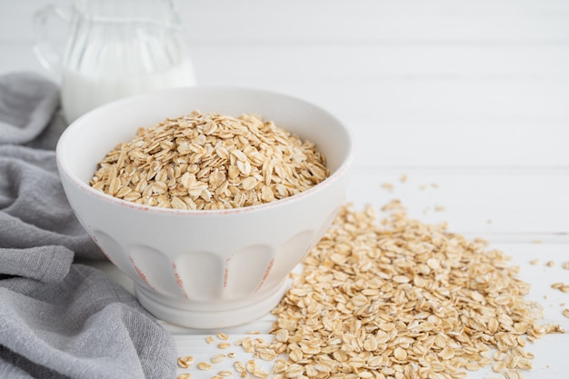 Raw dry oatmeal flakes in a bowl with milk on a white wooden background Healthy food Copy space