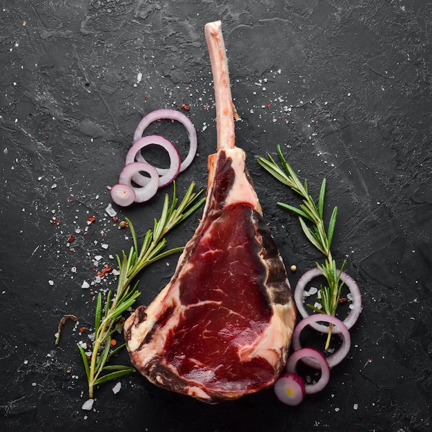 Raw dry steak on bone Tomahawk steak on a black stone background Top view Free space for your text