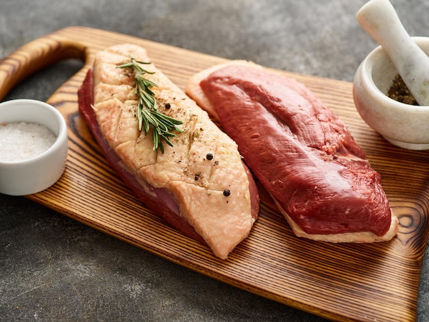 Raw duck breast pieces garnished with rosemary on wooden board