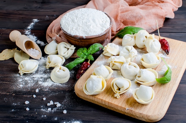 Raw dumplings with meat with flour on dark background 