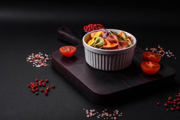 Raw farfalle pasta in different colors on a dark concrete background