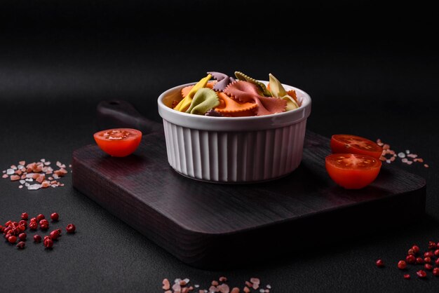 Raw farfalle pasta in different colors on a dark concrete background