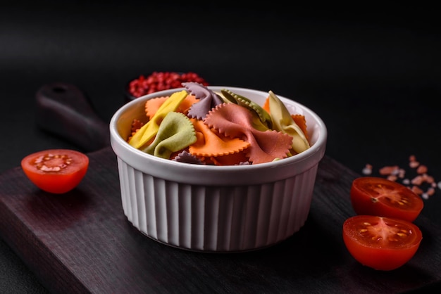 Raw farfalle pasta in different colors on a dark concrete background