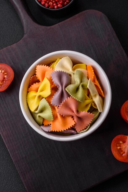 Raw farfalle pasta in different colors on a dark concrete background