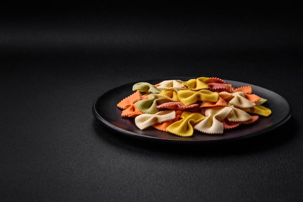 Raw farfalle pasta in different colors on a dark concrete background