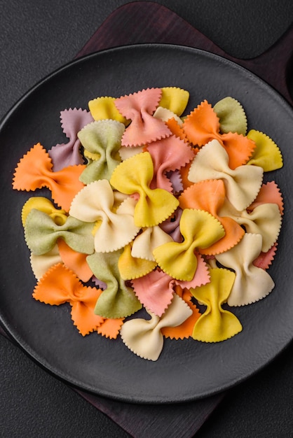 Raw farfalle pasta in different colors on a dark concrete background