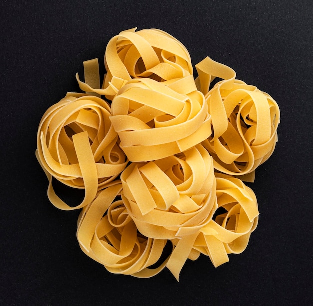 Raw fettuccine pasta isolated on black background top view