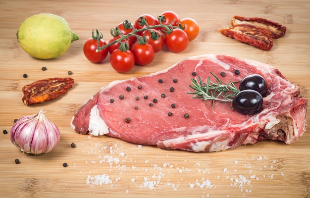 Raw fiorentina steak with spices and vegetables on a wooden table