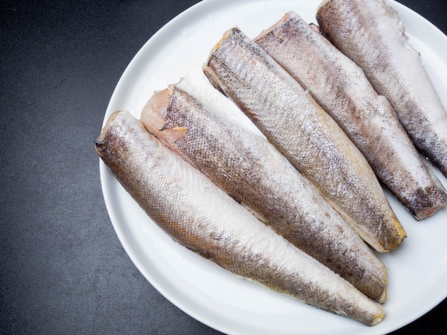 Raw fish hake on white plate on black background