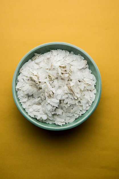 Photo raw flattened rice or thick or thin rice flakes for namkeen chivda snacks or aloo poha for indian breakfast, served in a bowl