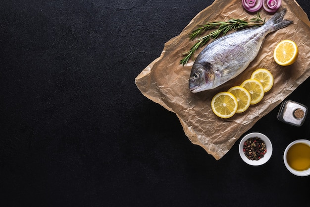 Raw Fresh Dorado Fish on cooking paper prepared for cooking with spices on a black background. Seafood. Top view. Copy space.