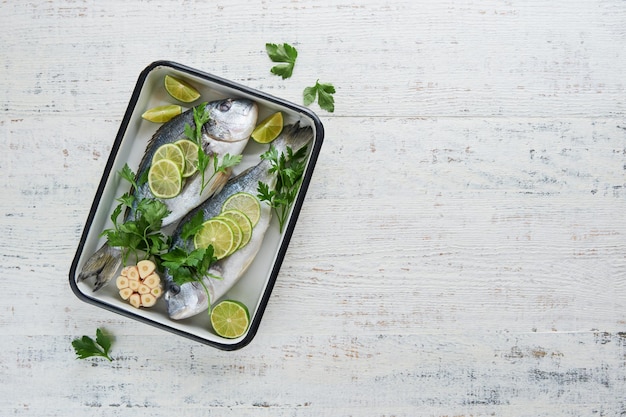 Raw fresh Fresh raw dorado with lemon lime parsley and salt on old wooden white background ready for cooking Sea bream dorado Seafood healthy food Top view Long banner format