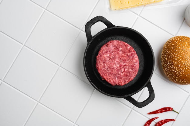 Raw fresh large beef burger on white ceramic squared tile table background top view flat lay with copy space for text