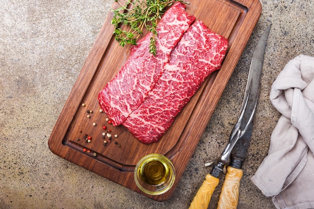 Raw fresh marbled meat Beef Steak and seasonings on cutting board over stone surface, top view