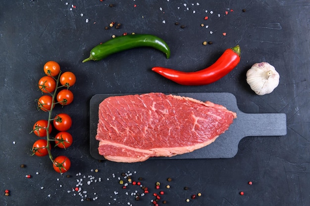 Raw fresh marbled meat and seasonings on dark background top view