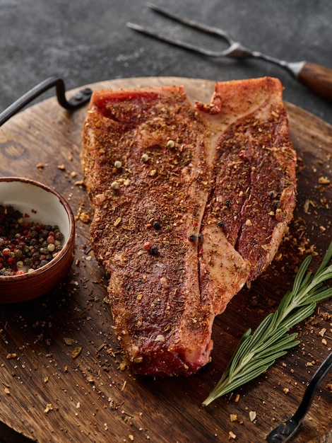 Raw fresh meat Tbone steak seasoning on chopping cutting wooden board on grey background