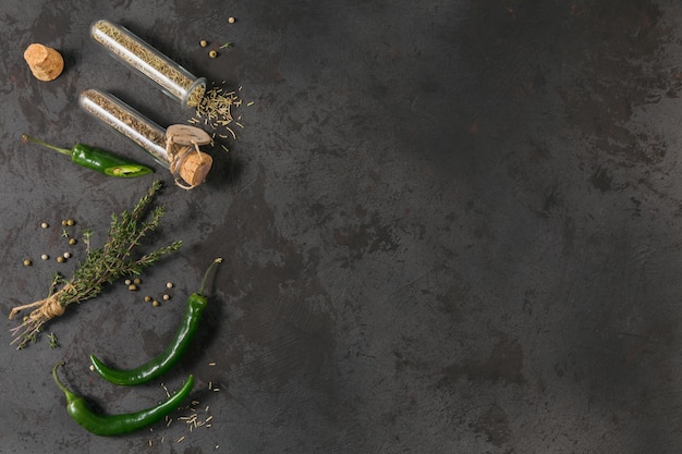 Raw fresh organic green chili pepper and assorted spices on black background Rosemary and basil in glass flasks Seasonings for food frame