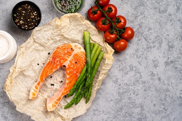 Raw fresh salmon steak and asparagus with tomato branch on parchment