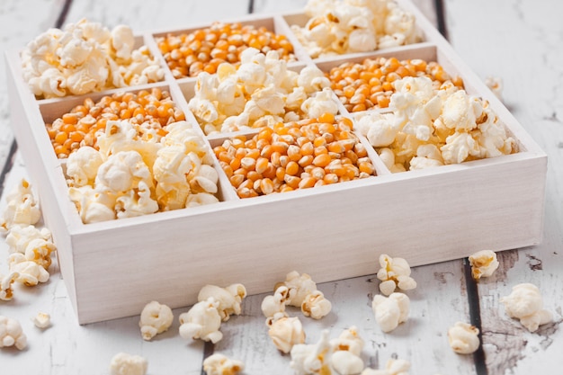 Raw golden sweet corn seeds and popcorn in white wooden box on light background