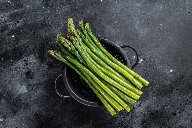 Raw green asparagus in a old colander. Black background. Top view.