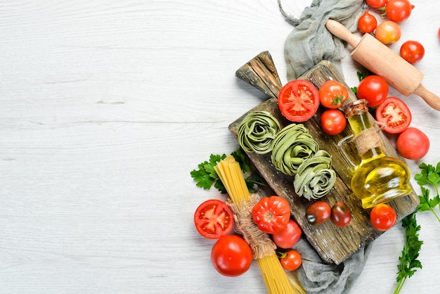 Raw green pasta with tomatoes oil and parsley on white wooden background Italian traditional cuisine Fresh vegetables Top view Free space for your text