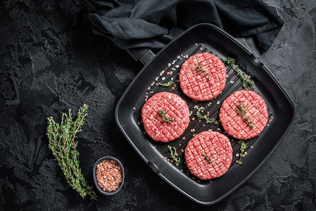 Raw Ground beef meat Burger steak cutlets in grill skillet ready for cooking Black background Top view