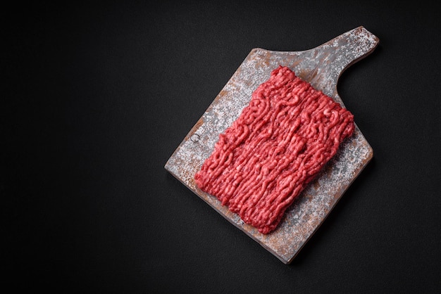 Raw ground beef or pork on a wooden cutting board with spices and salt