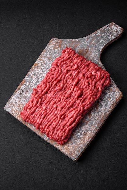 Raw ground beef or pork on a wooden cutting board with spices and salt