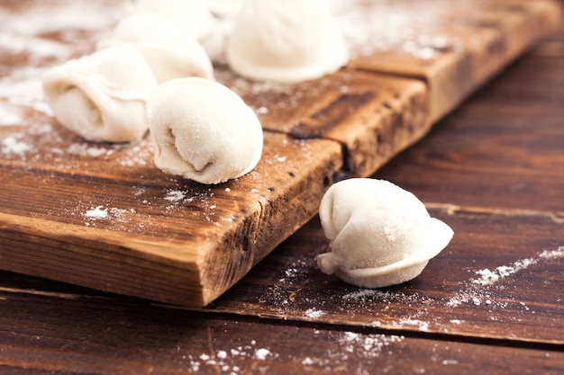 Raw homemade handmade pelmeni (dumplings) with meat on wooden background