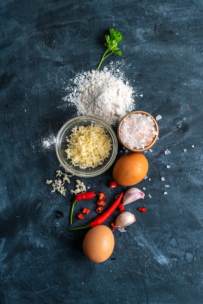 Raw ingredients for cooking on the table, cheese, salt, pepper, egg and different vegetables on a dark tables