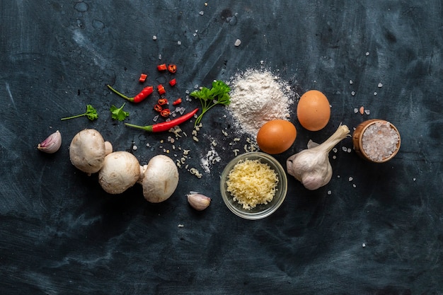 Raw ingredients for cooking on the table, cheese, salt, pepper, egg and different vegetables on a dark tables