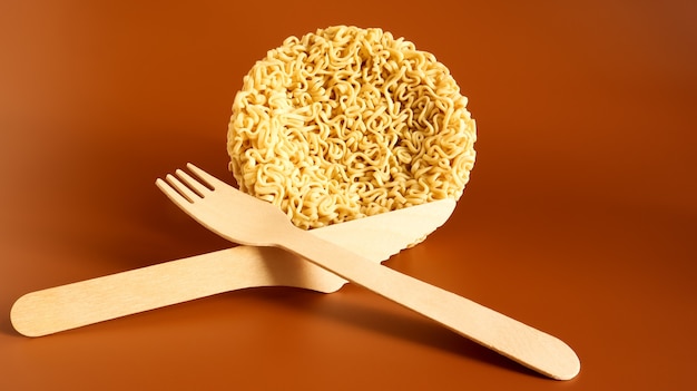 Photo raw instant noodles in the shape of a circle with a wooden disposable fork. pasta, for the preparation of which it is enough to pour boiling water and wait a few minutes. spaghetti. copy space.