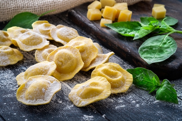 Raw Italian ravioli pasta with parmesan and basil on a wooden board with flour