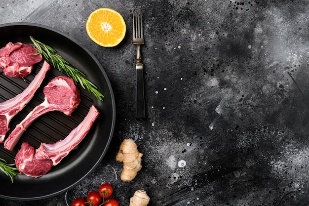 Raw lamb meat chops steaks set on frying cast iron pan on black dark stone table background