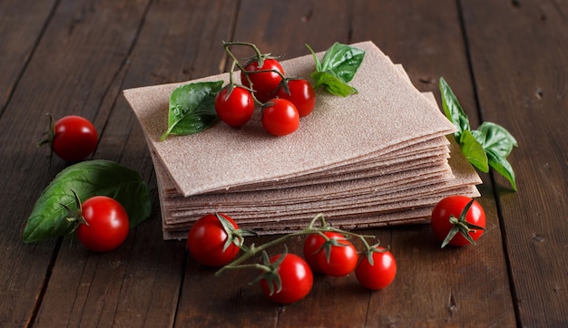 Raw lasagna sheets, basil and cherry tomatoes on a wooden table close up