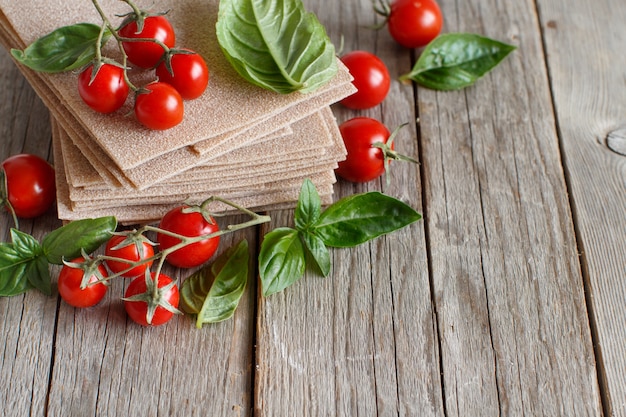 Raw lasagna sheets,basil and cherry tomatoes on a wooden table