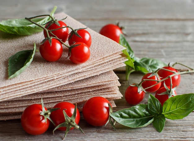 Raw lasagna sheets,basil and cherry tomatoes on a wooden table