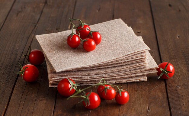 Raw lasagna sheets and cherry tomatoes on a wooden table