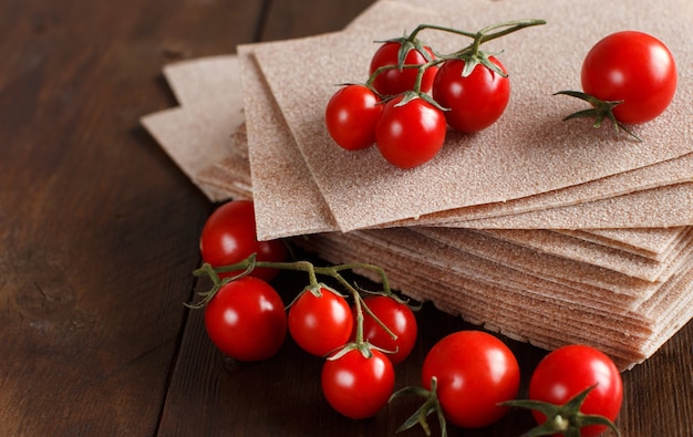 Raw lasagna sheets and cherry tomatoes on a wooden table