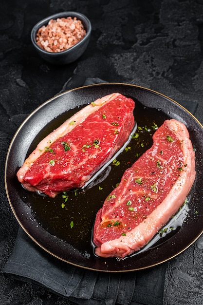 Raw marbled beef meat steak marinated with olive oil thyme salt and pepper Black background Top view