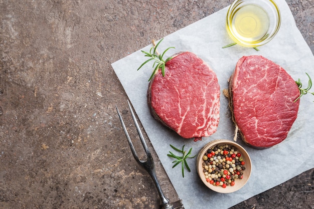 Raw marbled meat steak Filet Mignon with seasonings over stone background, top view.