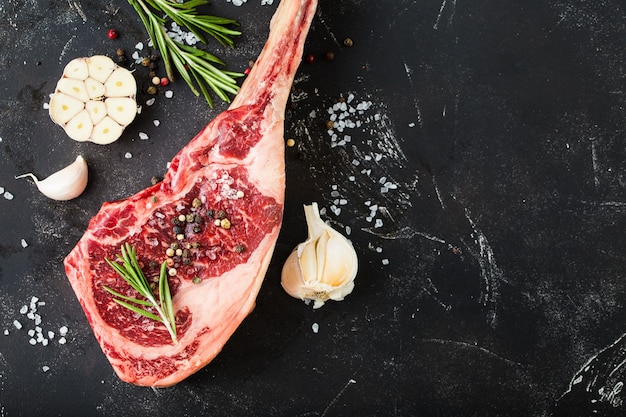 Raw marbled meat steak, seasonings, stone background.