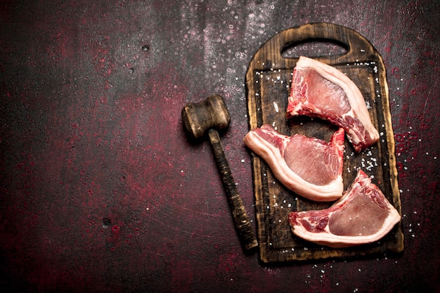 Raw meat background. Raw pork is with the old hammer. On rustic metal background.