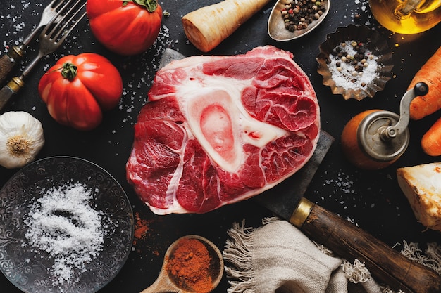 Raw meat beef steak with bone and vegetables spices on dark surface